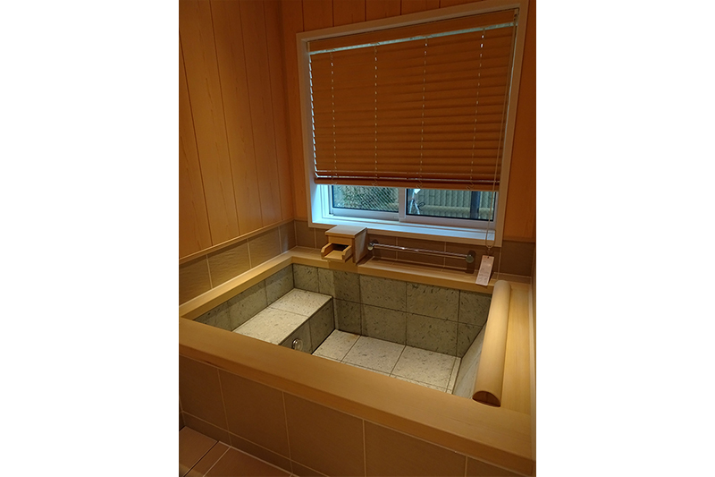 お客様が1番こだわった浴槽です。浴槽に浸かりながら庭を眺めるためのステップとヘッドレストも天然の木を使用しています。框は、天然カナダヒノキ材を使い、浴槽の中は、天然十和田石を使用しています。浴槽にお湯が溜まると、十和田石は綺麗なエメラルドグリーンに見えます。