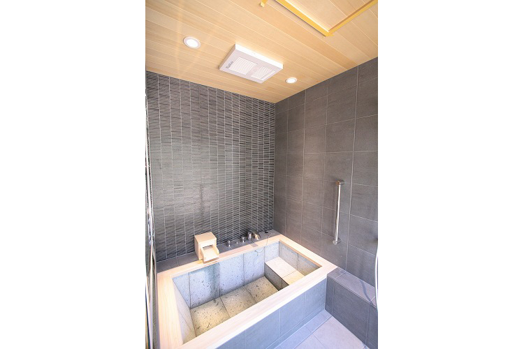 天井には、暖房乾燥換気扇付で、冬場のヒートショック対策に。天井も天然ヒノキ材を採用しています。ダークな色合いのタイルとヒノキがとてもマッチしています。
