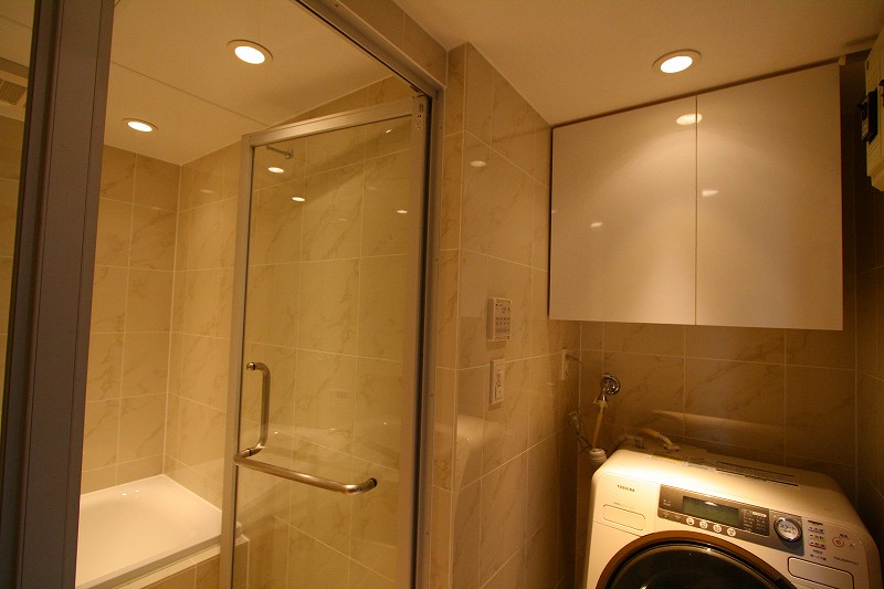 洗面室のリフォームも同時に行いました。洗面室の壁の仕上げ材も、浴室と同じ大理石調（ビアンコカラーラ）のタイルで仕上げました。浴室を洗面室のバスルーム空間のデザインの一体化できました。透明のガラスの間仕切りドアで一体感をより感じることが出来ます。